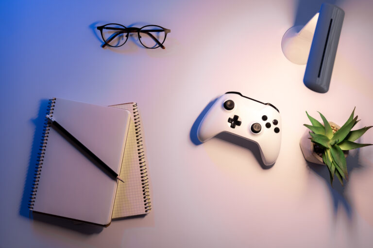 Vista superior de un escritorio de trabajo B2B con control de Xbox blanco, libreta de notas, lentes y planta suculenta, iluminado con tonos azules y blancos en Zapopan, Guadalajara, representando la planificación estratégica de marketing para videojuegos de la agencia Nibel.